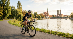 A professional, high-quality editorial shot of a cyclist riding along a scenic, sunlit riverside pat
